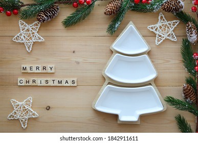 Empty Christmas Or New Year's Plate In White In The Shape Of A Christmas Tree On A Wooden Background Among The Branches Of A Fir Tree, Decorative Stars And The Inscription:merry Christmas. Top View. 