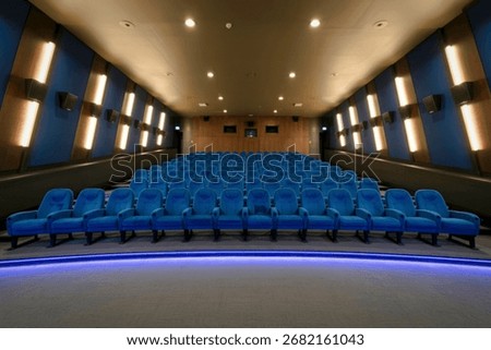 An empty cinema hall features rows of plush blue velvet seats arranged on tiered flooring