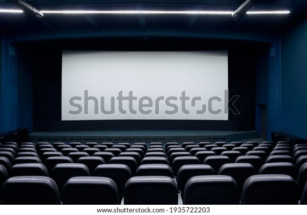 Empty cinema hall with screen and\
black row chairs. Concept of empty modern movie\
theatre.