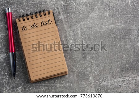 Empty circular notebook with brown sheets of paper on a concrete gray background and a red and silver elegant ballpoint pen and to do list