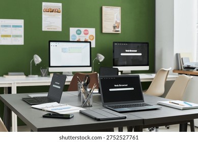 Empty classroom with multiple laptops, tablets, and desktop computers arranged on tables, digital devices displaying web browsers, educational materials suggesting computer literacy course setting