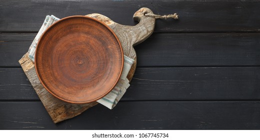 Empty clay dish on rustic cutting board over black wooden background