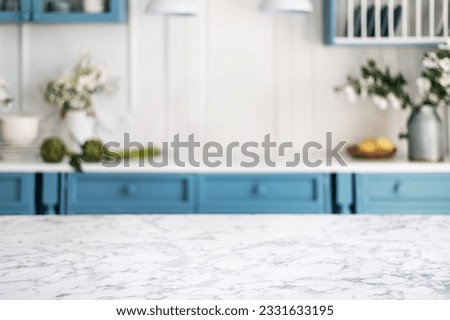 Empty and clean marble dining table in scandinavian kitchen. Modern monochrome interior with blue drawers on wooden furniture. Tablewear and vases with flowers.