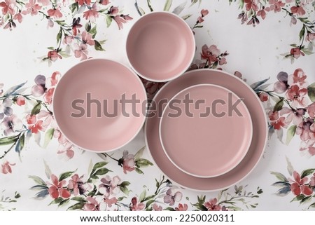 Empty clean plates on a white tablecloth with floral pattern, table top view. Flat lay, minimalistic design. Pink ceramic crockery. Trendy tableware set for serving and eating meals. Beige dishes.