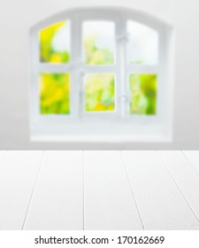 Empty clean white kitchen table in front of a cottage pane arched window with a view of greenery in summer sunshine as a background for product placement