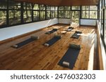 Empty clean yoga gym room studio interior with big windows mats on wooden floor. Place for yoga exercises group meditation practices retreats sessions background in natural forest garden area building