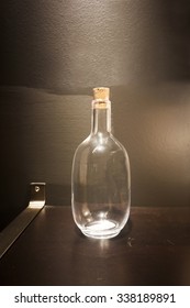 Empty Clear Bottle On Wooden Bar With Light On Black Background. 