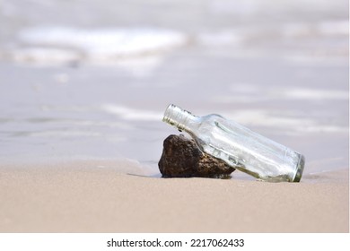 Empty Clear Glass Bottle Draped Over Small Rock On The Beach And Square Shape Bottle There Is Space On The Left Or Garbage On The Beach Select Focus Of Bottle Head