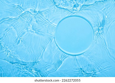 Empty clear glass circle podium on blue transparent calm water texture with waves in sunlight. Abstract nature background for product presentation. Flat lay cosmetic mockup, copy space.