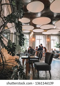 Empty Closed Restaurant. No Guests.waitress Girl In Luxury Modern Interior Cafe Serve Menu To Foreign Tourist In Cozy Lunch Place, New Fashion Furniture And Green Flowers.20.08.2018, Tbilisi, Georgia.