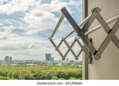 Empty Clothes Folded Dryer Rack Hanging On The Wall In Balcony Of Residential Building With Park And Sky Background