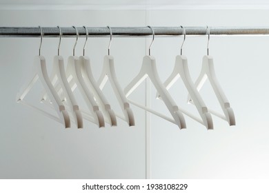 Empty Clothes Hangers, Closeup. Modern New White Closet. Many Wooden White Hangers On A Rod. Store, Sale, And Design Concept. Place For Text.