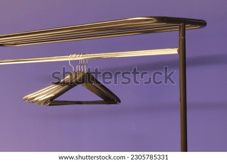 an empty coat rack with several black hangers on a black bar, and a blue wall in the background