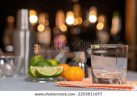 Empty cocktail glass standing on the steel bar counter on the blurred dark and light background. Ingredients for a cocktail
