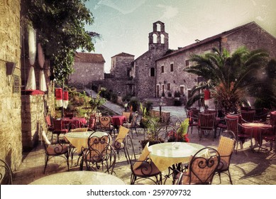Empty coffee terrace with tables and chairs in old town of Budva on sunny day at sunset, Montenegro. Filtered image, vintage effect applied. Grunge