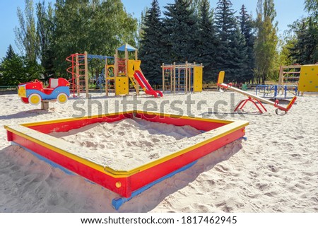 Empty colorful children playground set in park. Sandbox on foreground. Playground set with no children. Play yard with sandbox, balance and other playground elements. Outdoor playground. Sandy ground