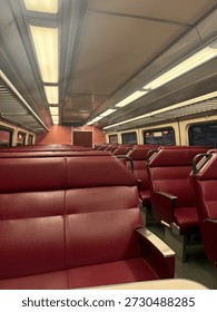 Empty commuter train interior with rows of red seats and overhead lighting, photographed from a passenger’s perspective. vacant public transportation setting with no people present. 