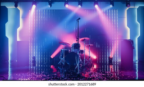 Empty Concert Stage In A Night Club. Professional Drum Kit And Other Music Equipment For Live Gig With Rock Band. Confetti On The Dance Floor. Bright Colorful Strobing Lights On Stage.