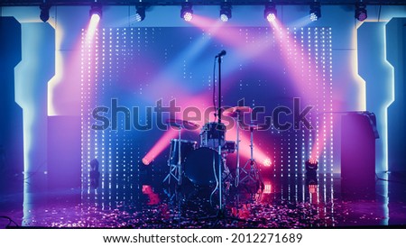 Empty Concert Stage in a Night Club. Professional Drum Kit and Other Music Equipment for Live Gig with Rock Band. Confetti on the Dance Floor. Bright Colorful Strobing Lights on Stage.