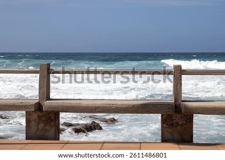 Empty concrete benches on the coast of Atlantic ocean. Big waves in the winter. Blue sky with white clouds. El Agujero, Las Palmas, Gran Canaria, Canary Islands, Spain.