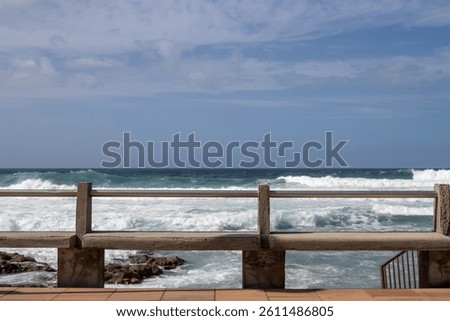 Empty concrete benches on the coast of Atlantic ocean. Big waves in the winter. Blue sky with white clouds. El Agujero, Las Palmas, Gran Canaria, Canary Islands, Spain.