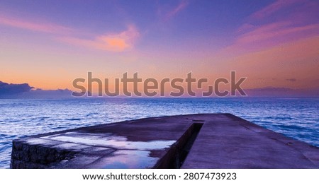 Empty concrete pier extending into Atlantic Ocean at pre-dawn, purple-to-peach gradient sky, calm sea, Madeira.