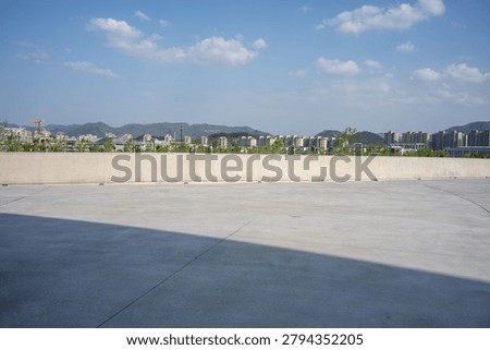 Empty concrete rooftop terrace with distant city skyline and mountains under blue sky
