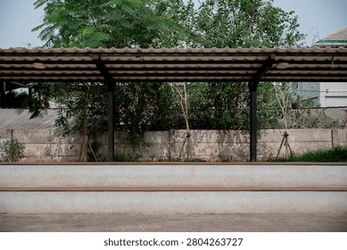 Empty concrete stepped seating under a metal roof shelter in an outdoor public park area