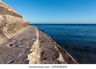 Empty concrete steps leading down to the Atlantic Ocean shoreline with calm seas at sunset in Cascais in Portugal - Powered by Shutterstock