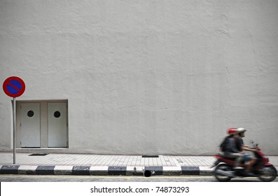 An empty concrete wall with copyspace for text along a street with a motorbike driving by.