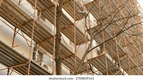 An empty construction site features scaffolding around a block of flats. Workers are preparing the building for insulation and renovation to enhance thermal efficiency.