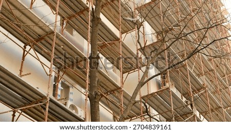 An empty construction site features scaffolding around a block of flats. Workers are preparing the building for insulation and renovation to enhance thermal efficiency.