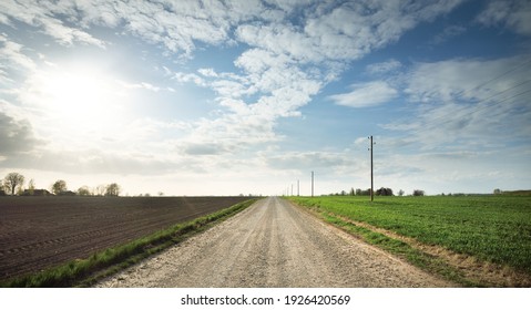 An empty country road through the plowed fields. Dramatic sky. Europe. Transportation, logistics, communications, driving, off-road, remote places. Concept landscape. View from the car