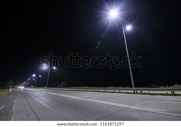 Empty\
countryside road at night with street lights.\
