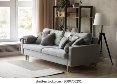 Empty Cozy Comfy Grey Couch Furniture In Renovated Living Room In Modern Rent House Or Apartment. Comfortable Sofa With No People In New Own Home. Renovation, Interior Design Concept.