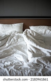 Empty Crumpled White Bed With A Blanket And Pillows In A Dark Room In The Morning. Family Life Concept.