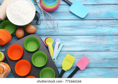 Empty cupcake cases with different kitchen utensils on wooden table