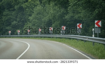 Empty curved forest road lined with chevron signs and guardrail