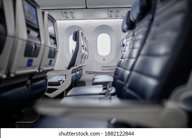 Empty dark blue seats with screens in the back inside airplane with windows as background. Peaceful and tranquil row of seats in commercial plane cabin. Airplane interiors