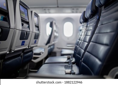 Empty dark blue seats with screens in the back inside an airplane with windows as background. Peaceful and tranquil row of seats in commercial plane cabin. Airplane interiors
