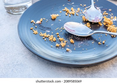 Empty Dark Plate With Crumbs And Dirty Spoon On A Table After Sweet Pie.