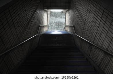 Empty dark underpass perspective. Stone stairs go down to the light. Abstract night city background 