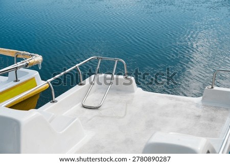 Empty deck of a modern white pleasure boat or catamaran parked on calm blue water, summer vacation and nautical travel background.