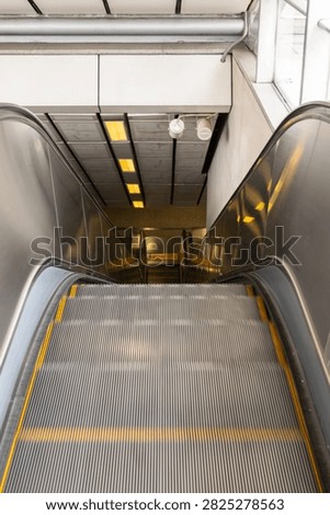 Empty descending escalator inside a modern public transit station with metal steps handrails and indoor lighting representing transportation infrastructure and urban mobility