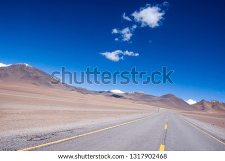 empty desert highway surrounded by mountains with a clear blue sky