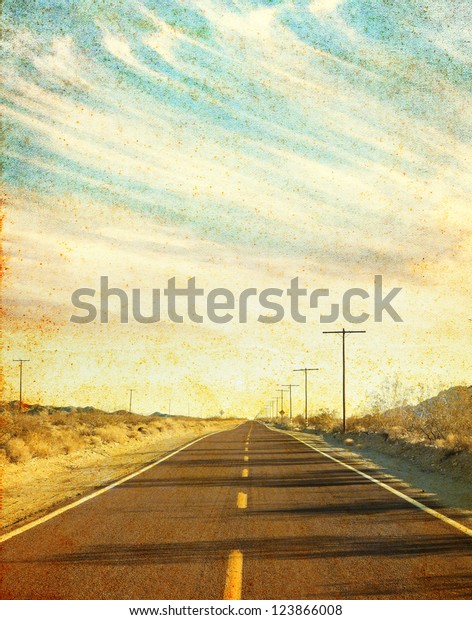 An empty desert road in Arizona\'s Mojave desert\
with grunge stains and spots.  Image has a distinct paper texture\
visible at 100%.