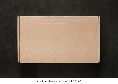 Empty Design Of A Brown Box On A Black Stone Concrete. Mock Upward View From Above Isolated. Packing Box. Cardboard Template Is Closed At The Top.