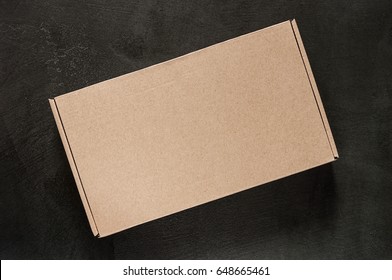 Empty Design Of A Brown Box On A Black Stone Concrete. Mock Upward View From Above Isolated. Packing Box. Cardboard Template Is Closed At The Top.