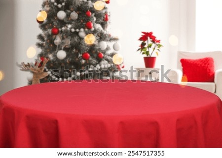 Empty dining table with red tablecloth near Christmas tree in room