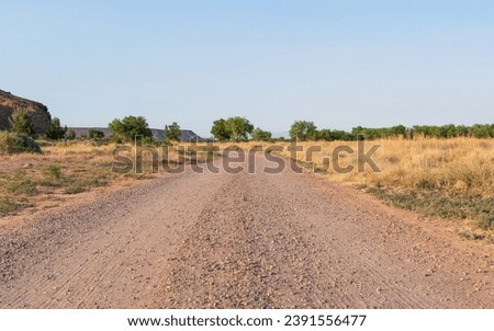 An empty dirt road bends out of sight near red rock mesas in the high desert countryside.